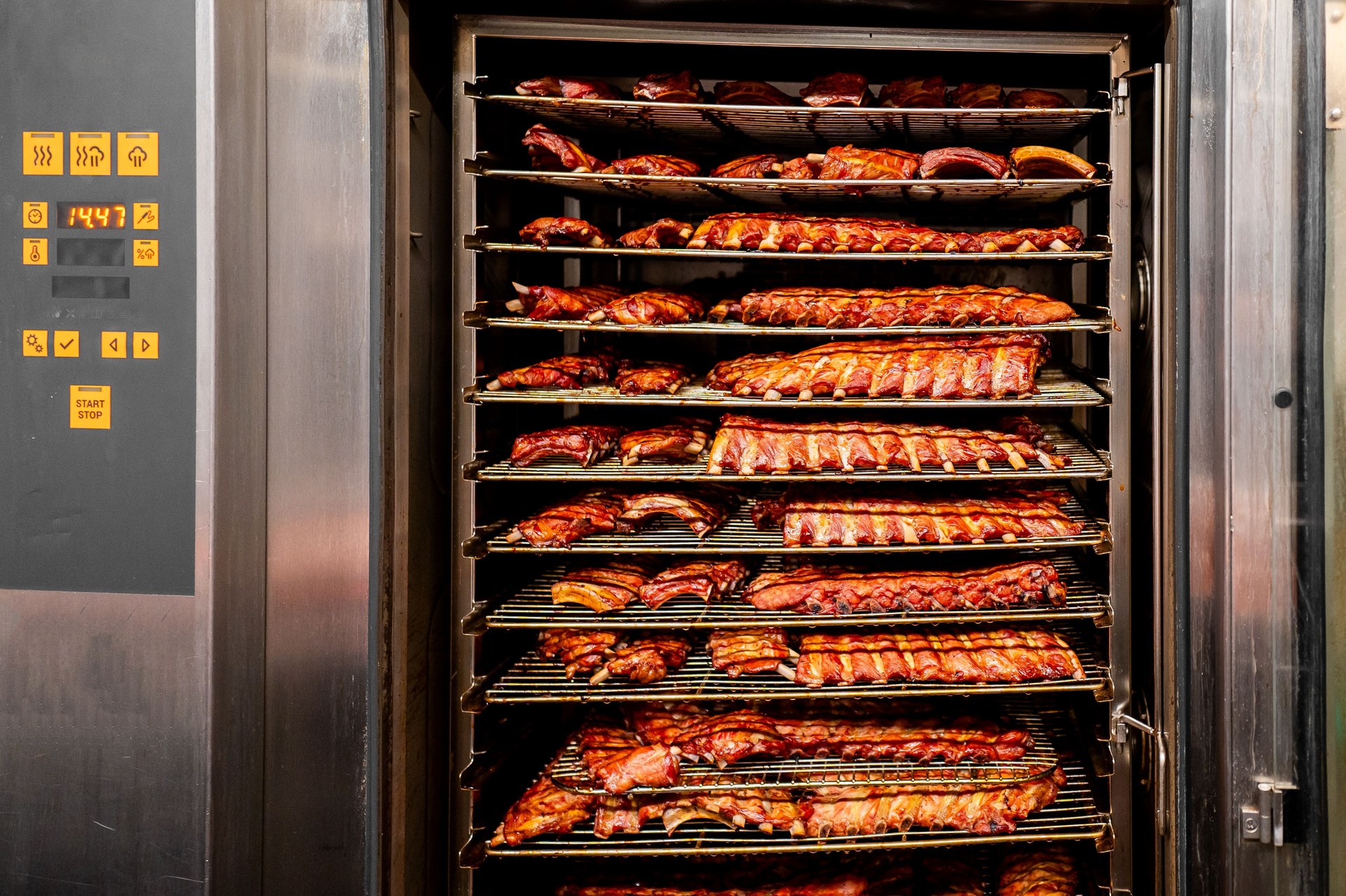 A commercial smoking oven filled with racks of smoked ribs, showcasing the culinary process in a professional kitchen setting. Perfect for food industry, culinary arts, and restaurant-related visuals.